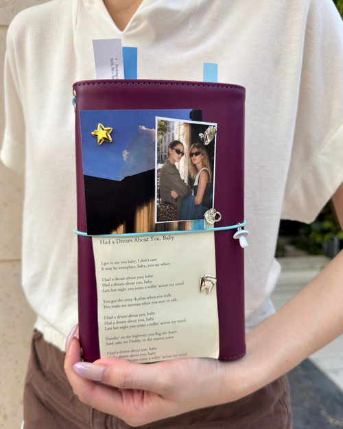 A person holds a Burgundy Full Size Journal styled with a powder-blue elastic band, blue mushroom charm, removable KEPT cover charms, photos, and layered paper keepsakes.