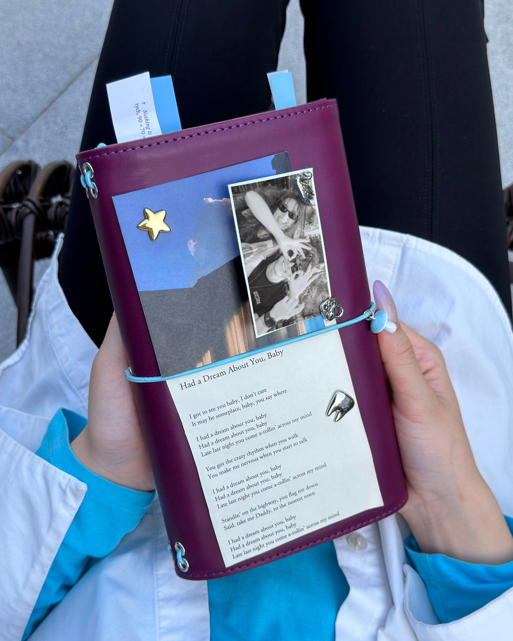 A person holds a Burgundy Full Size Journal decorated with a powder-blue elastic band, blue mushroom charm, removable KEPT cover charms, a portrait photo, and paper keepsakes.