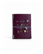 Burgundy Pocket Journal with a powder-blue elastic band and four removable KEPT cover charms on a white background.
