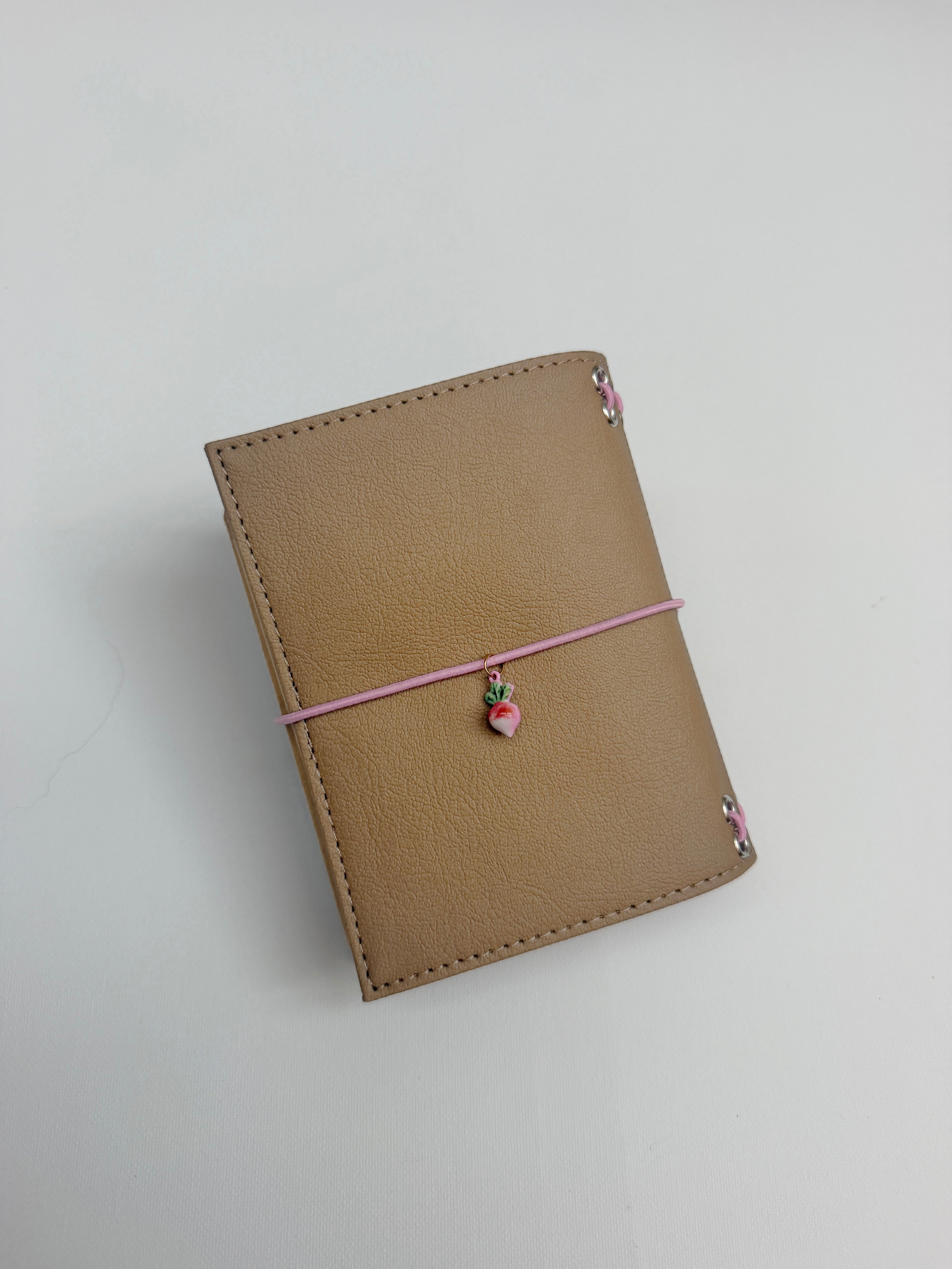 Back view of the Camel Radish Pocket Journal with a textured camel-colored PU cover and blush-pink elastic band.