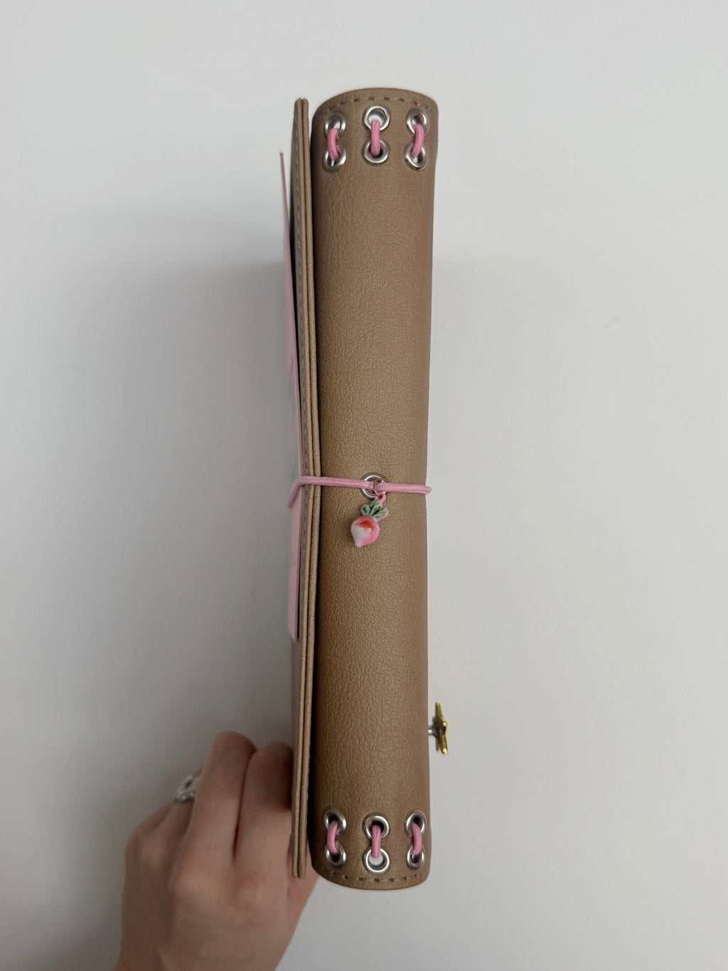 Side view of the Camel Radish Full Size Journal showing its textured PU cover, refillable inserts, blush-pink elastic band, pink radish charm, and metal eyelet binding on a white background.