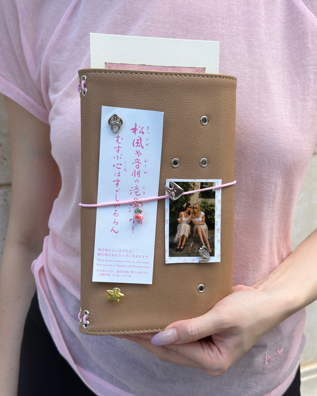 A person holds a Camel Radish Full Size Journal styled with a blush-pink elastic band, pink radish charm, four removable KEPT cover charms, a photo, and paper keepsakes.