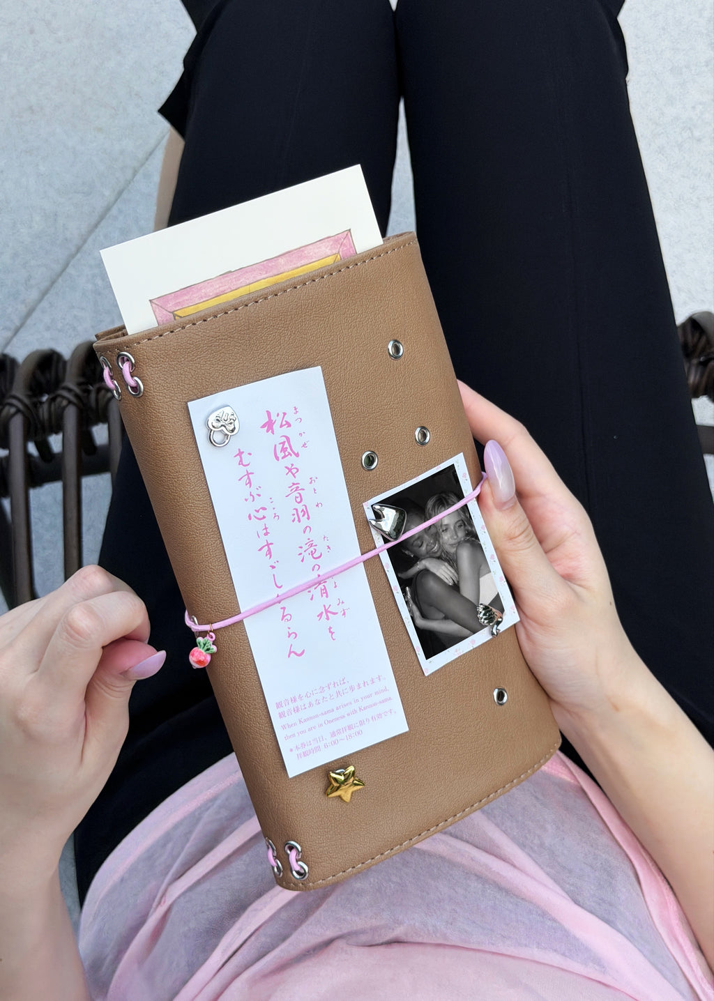 A person holds a Camel Radish Full Size Journal styled with a blush-pink elastic band, pink radish charm, removable KEPT cover charms, a photo, and paper keepsakes.