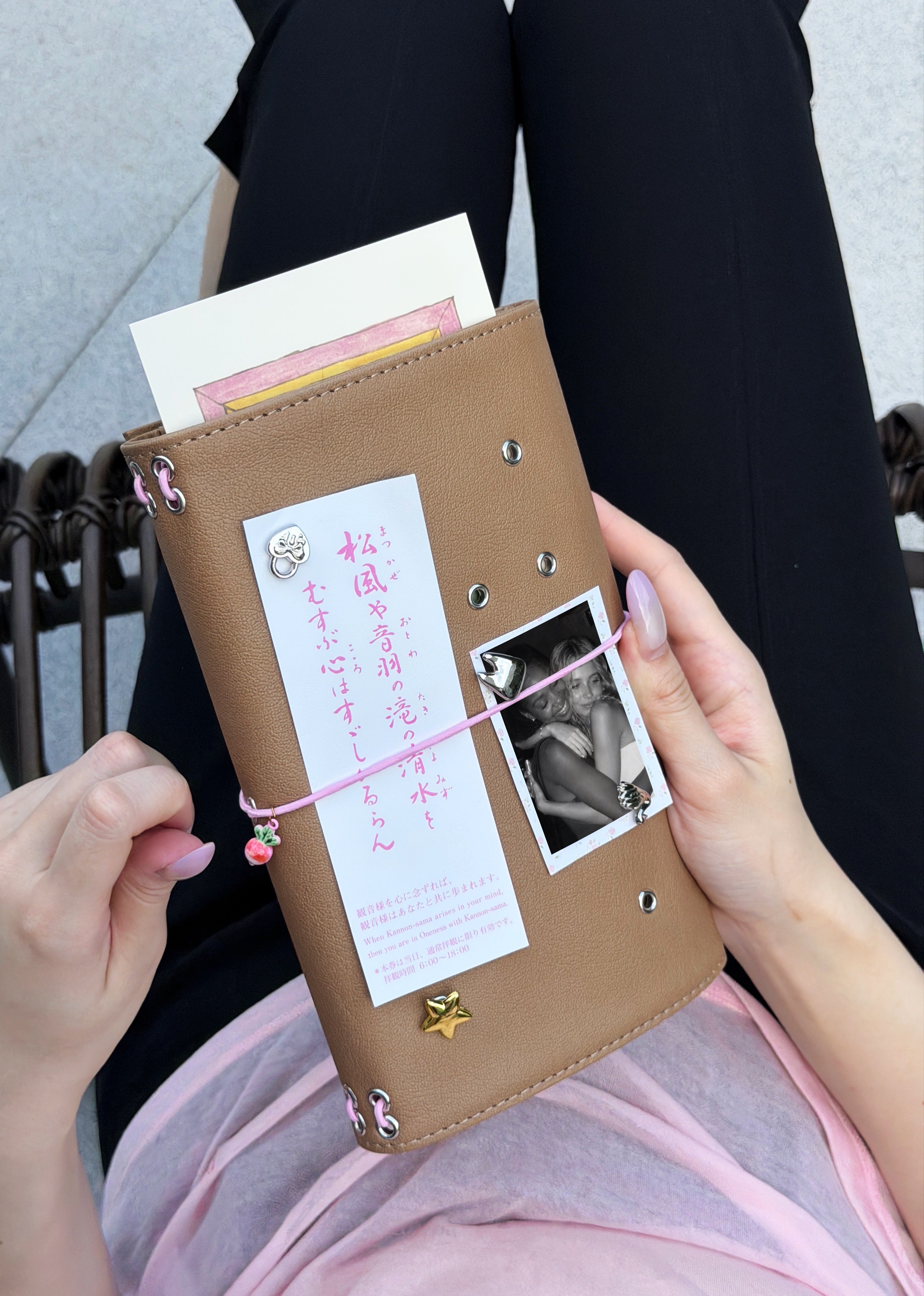 A person holds a Camel Radish Full Size Journal styled with a blush-pink elastic band, pink radish charm, removable KEPT cover charms, a photo, and paper keepsakes.