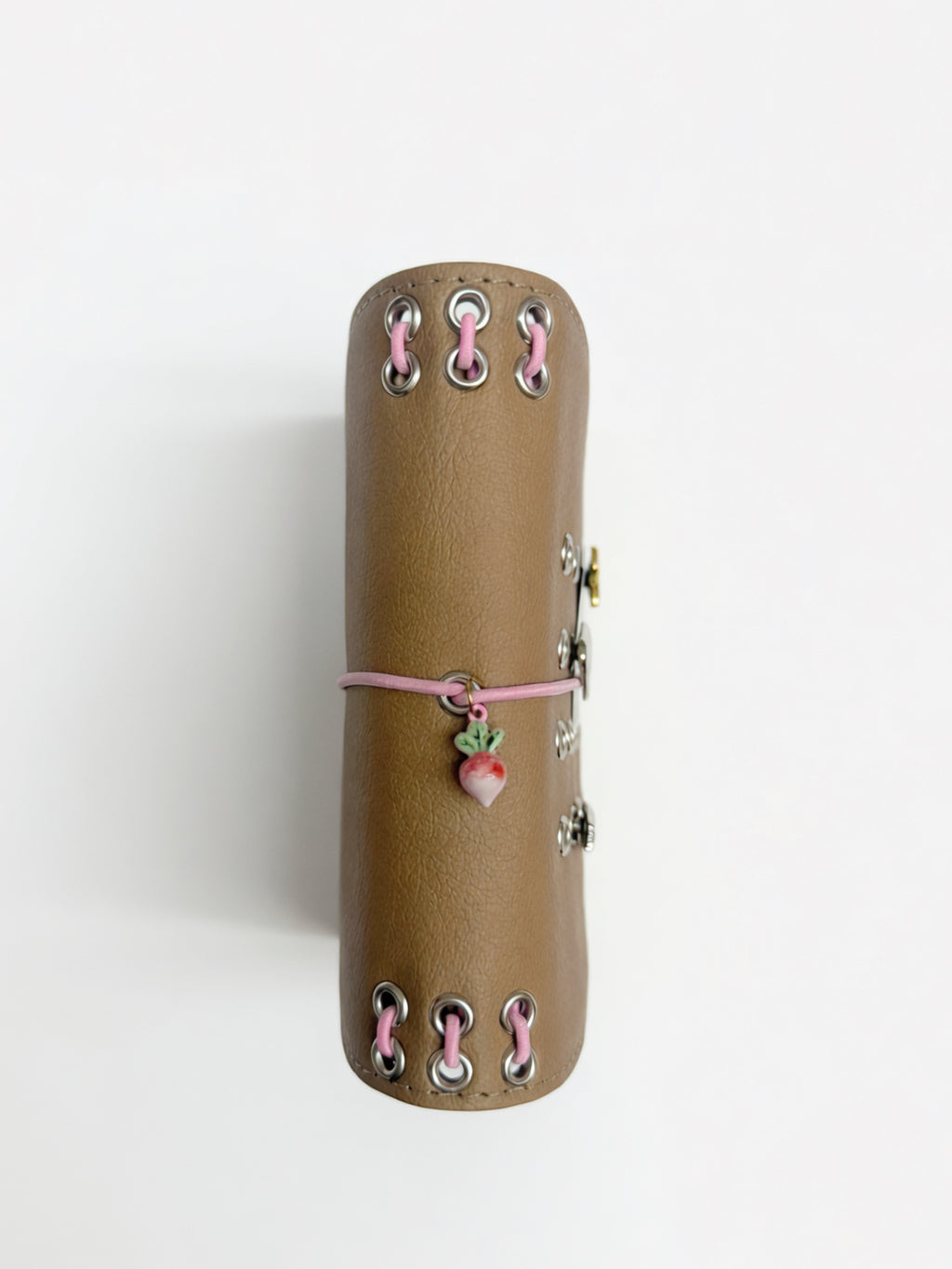 Spine view of the Camel Radish pocket journal showing pink lacing, metal eyelets, elastic band, and radish charm