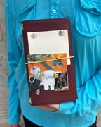 A person holds an Chestnut Fox Full Size Journal styled with a butter-yellow elastic band, fox charm, removable KEPT cover charms, a photo, and layered paper keepsakes.