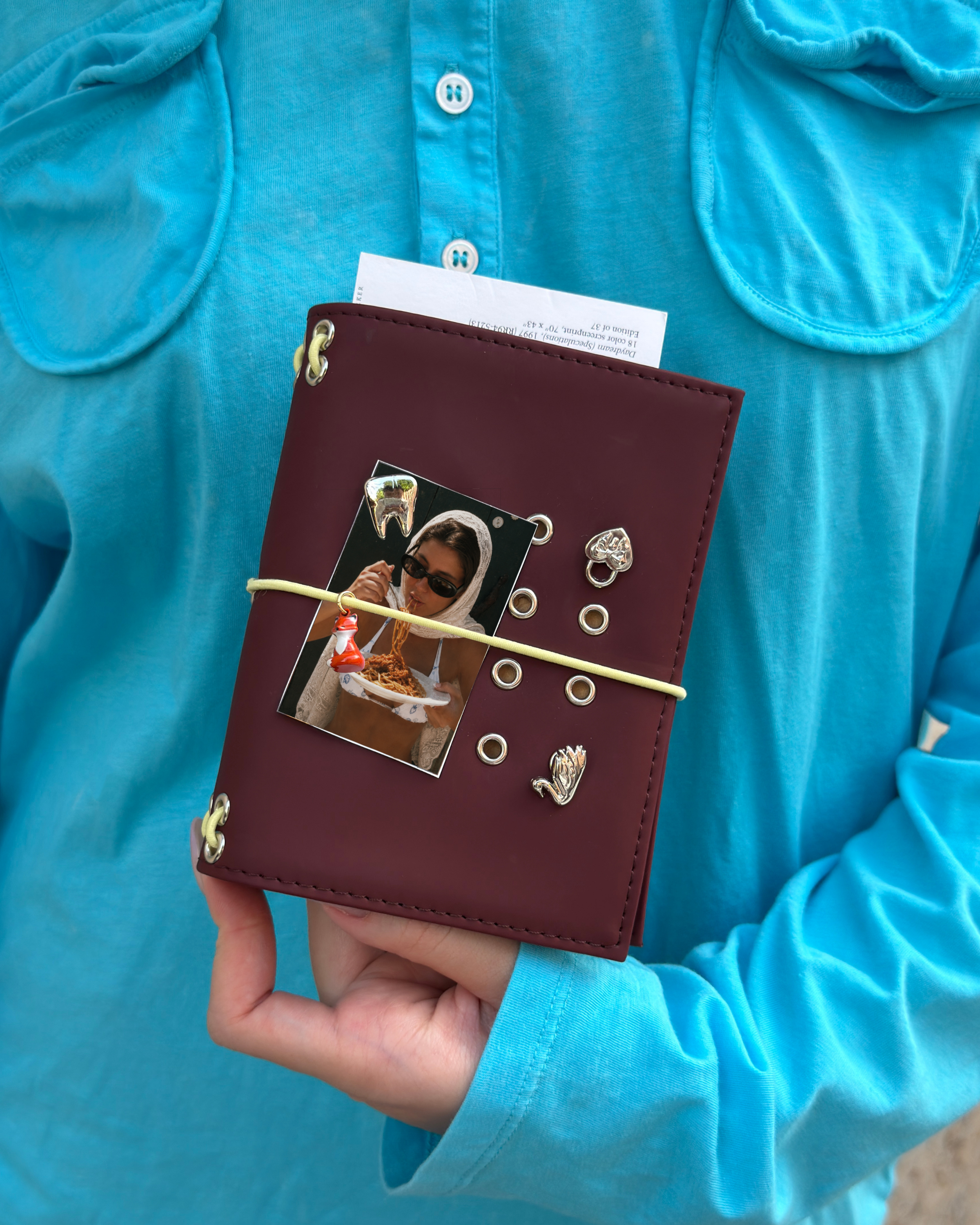 A person holds an Chestnut Fox Pocket Journal styled with a butter-yellow elastic band, fox charm, four removable KEPT cover charms, and a photo insert.