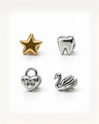 Four small metallic charms arranged on a clean white background: a gold star, a silver tooth, a silver heart-shaped padlock with a bow, and a silver swan.