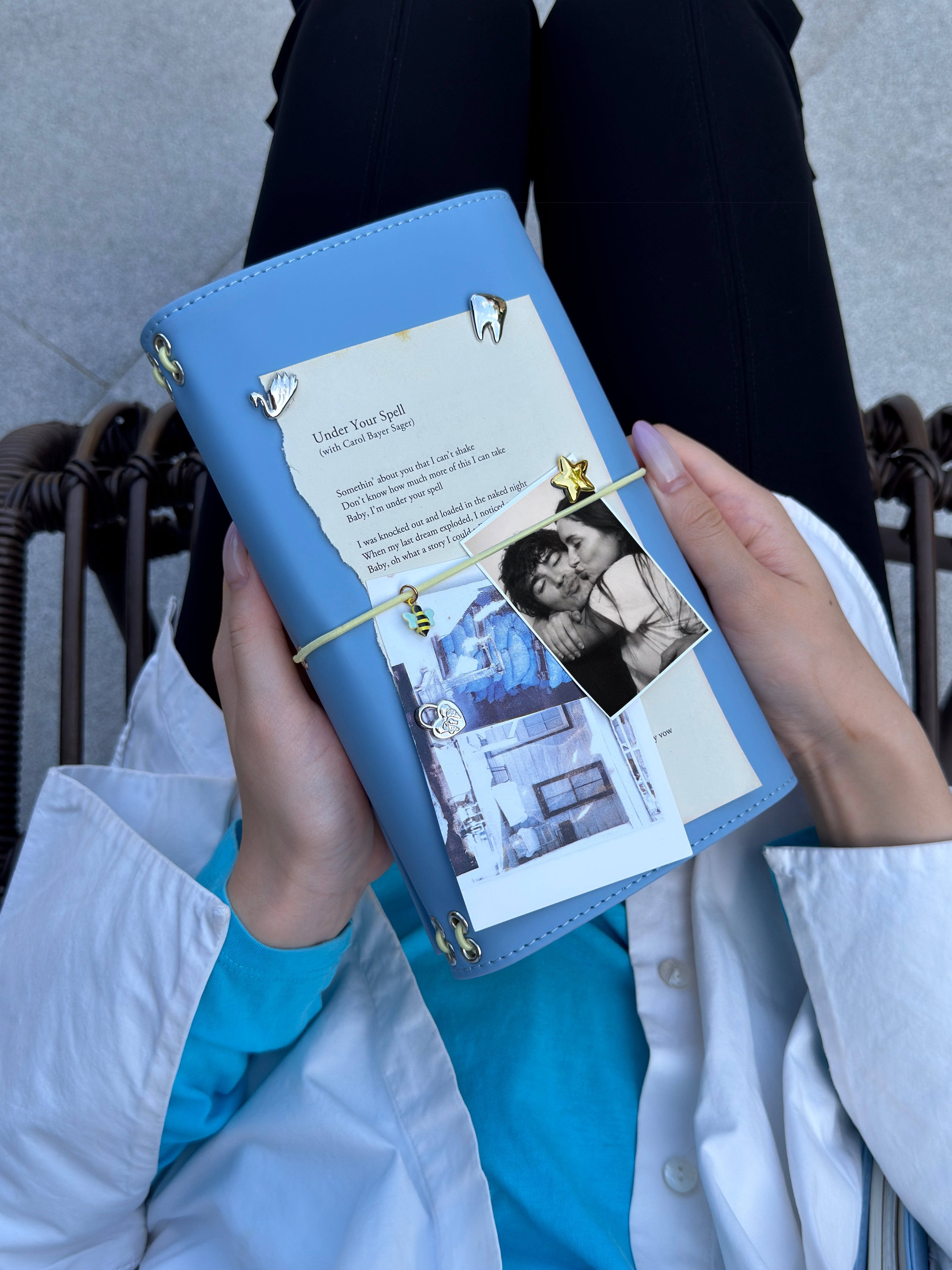 Person holding a mist blue full-size refillable journal decorated with removable metal charms, a black-and-white photo, and layered paper keepsakes.