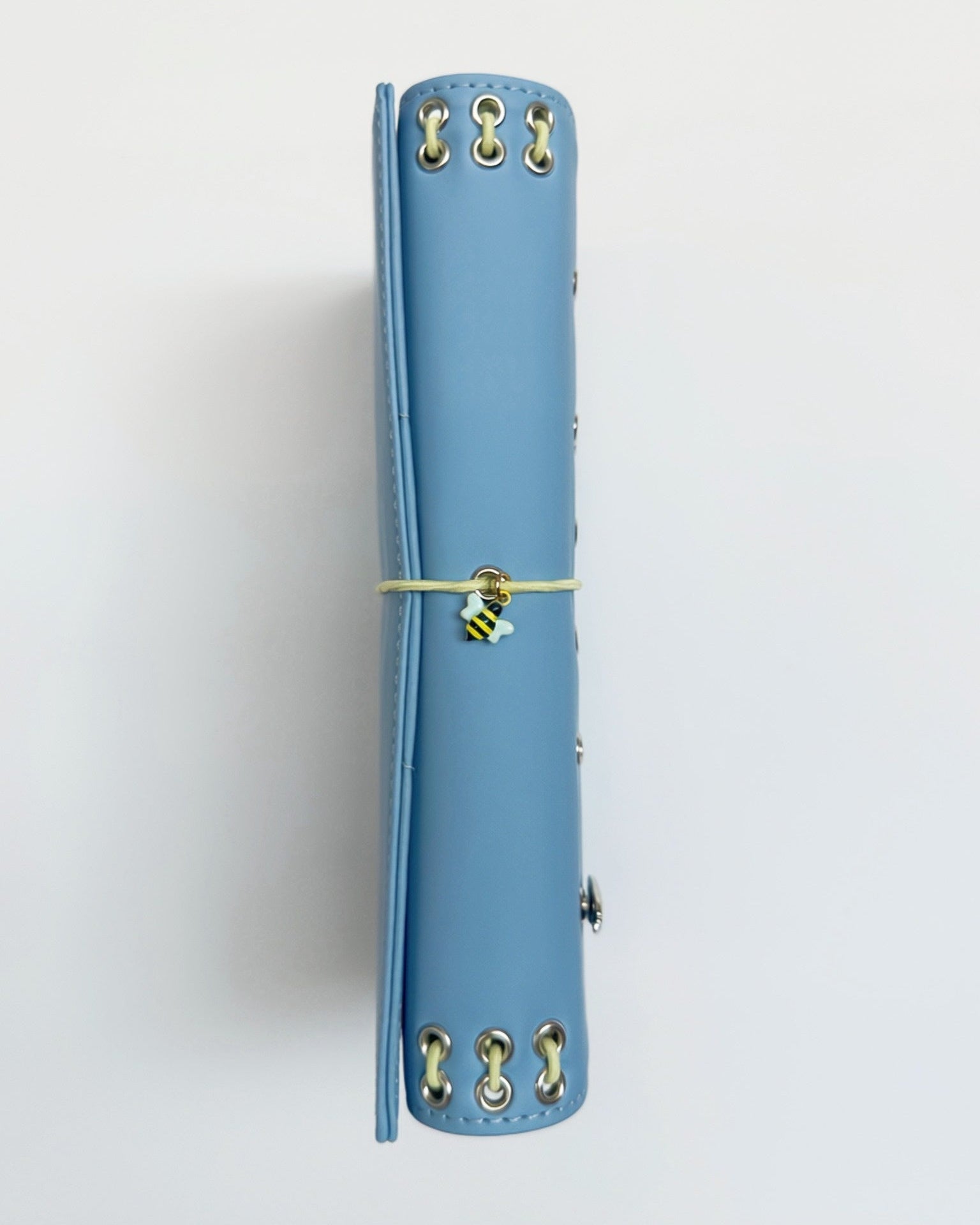 Spine view of the Mist Blue full size journal showing yellow lacing, metal eyelets, butter-yellow elastic band, and a bee charm.