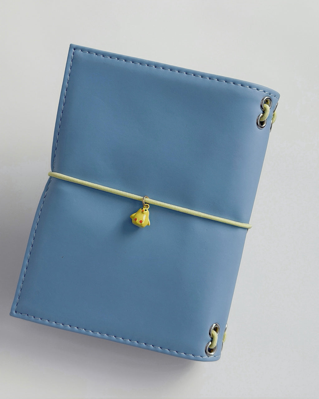 Back view of the Mist Blue pocket journal with a butter-yellow elastic band and yellow chick charm