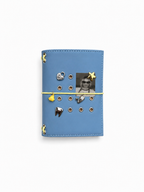 Mist Blue pocket journal with a butter-yellow elastic band, yellow chick charm, and removable KEPT cover charms