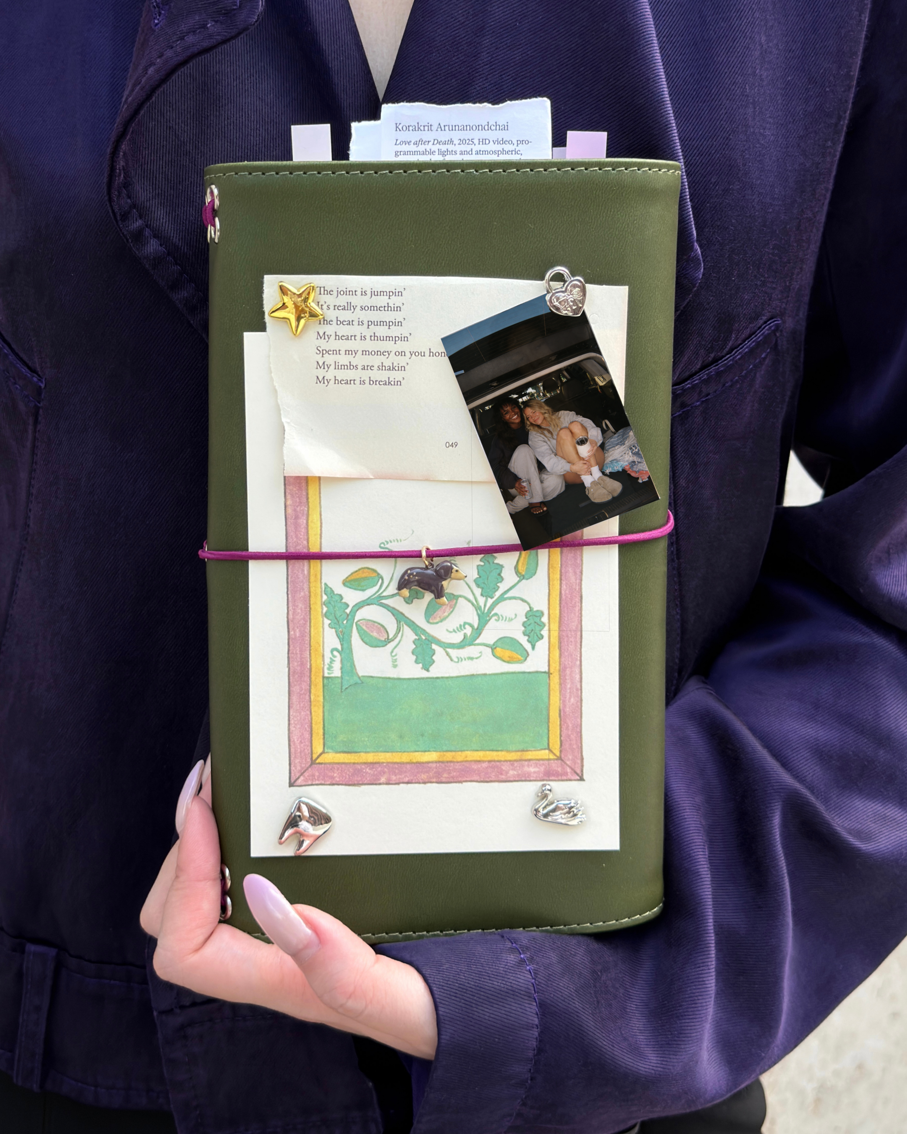 A person holds an Olive Full Size Journal styled with a burgundy elastic band, dachshund charm, removable KEPT cover charms, a photo, and layered paper keepsakes.