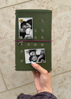 A hand holds an Olive Full Size Journal styled with a burgundy elastic band, dachshund charm, four removable KEPT cover charms, and two portrait photo inserts.