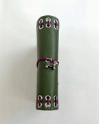 Side view of the Olive Pocket Journal showing its smooth PU cover, burgundy elastic band, dachshund charm, and metal eyelet binding on a white background.
