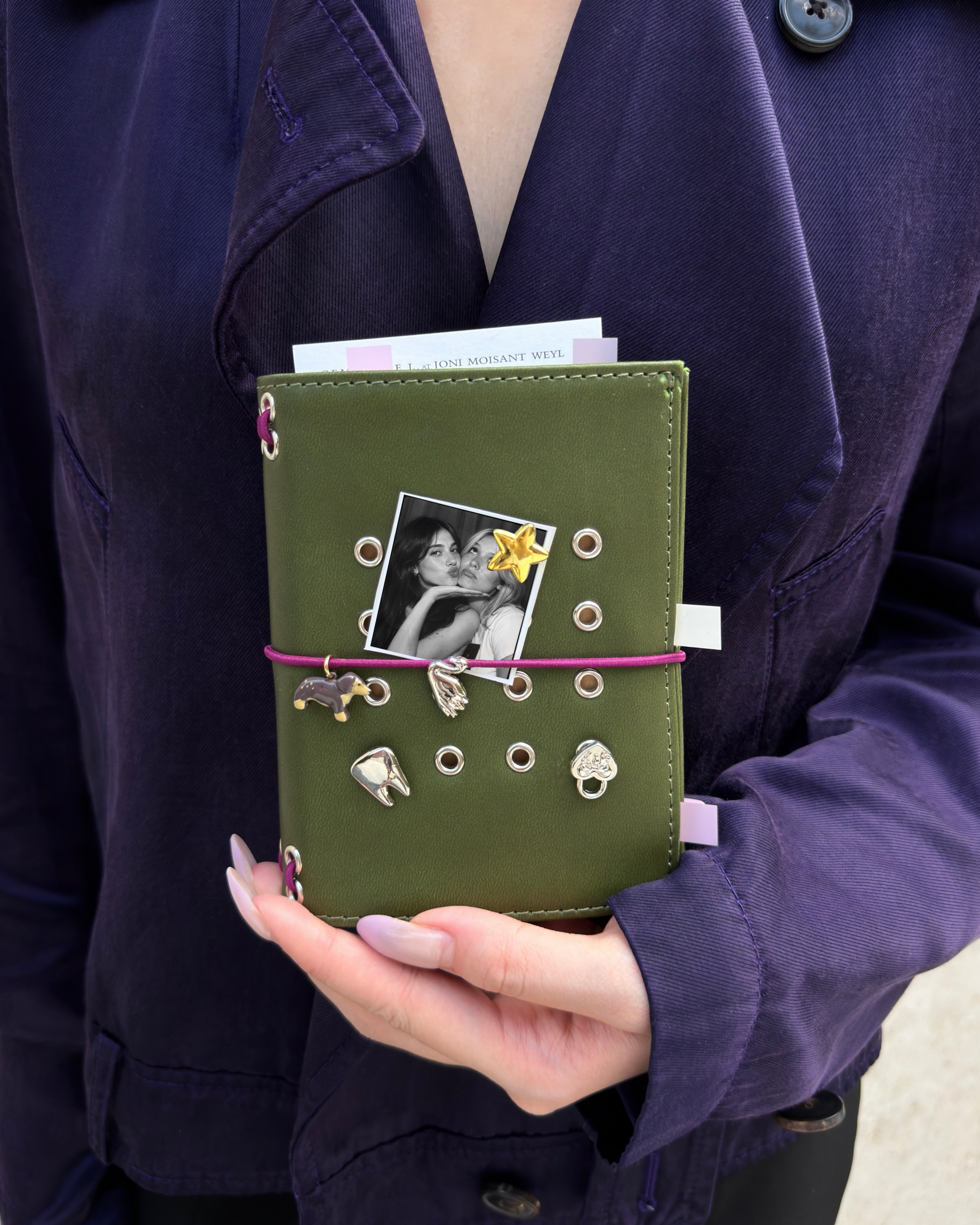 A person holds an Olive Pocket Journal styled with a burgundy elastic band, dachshund charm, four removable KEPT cover charms, and a black-and-white photo insert.