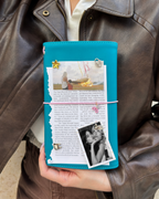 A person holds a Teal Full Size Journal styled with a blush-pink elastic band, removable KEPT charms, photos, and paper keepsakes.