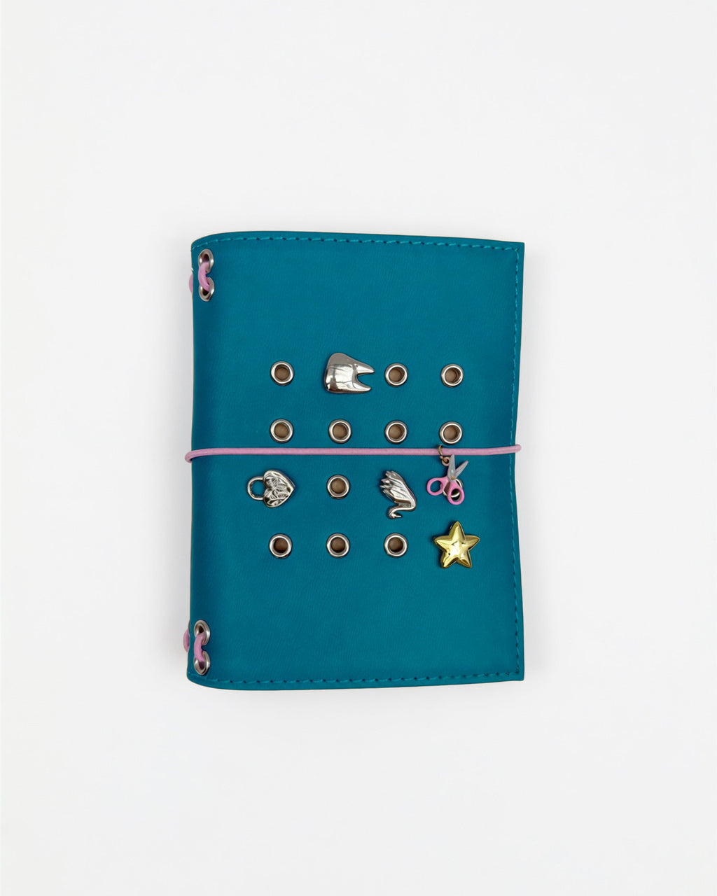 Teal pocket journal on a white background with a blush-pink elastic band, pink scissors charm, and removable KEPT cover charms.