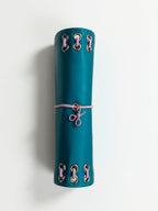 Spine view of the Teal pocket journal showing pink lacing, metal eyelets, elastic band, and scissors charm